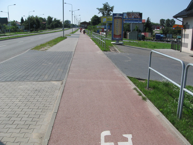 Przykład przebiegu DDRu przez wjazd do posesji w Radomiu. Mimo tego, że posesja znajduje się poniżej poziomu drogi, nie wprowadzono obniżenia przejazdu. Co więcej, krawężniki zostały umieszczone wzdłuż drogi rowerowej (źródło :rowerowytorun.com.pl)